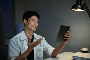 Asian businessman focus online video call meeting assignment on paperwork with colleague in tablet computer in office overtime at night