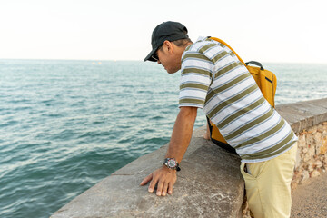 Mediterranean coastline view with Latin traveler resting against stone wall, enjoying seascape in...
