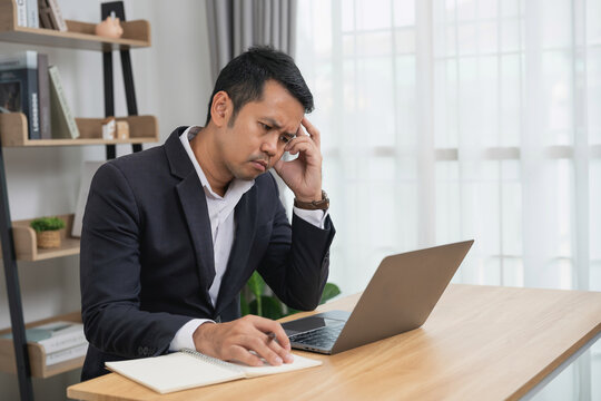 Thoughtful professional man working on laptop at a desk in a modern office, focused on solving problems and making decisions during a busy day.