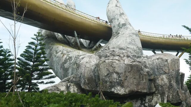 Golden bridge spanning mountainous landscape, supported by massive stone hands at ba na hills, vietnam, attracting visitors with dramatic architectural design