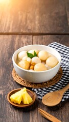 A bowl of sweet, light-colored spheres in a broth, accompanied by fresh pineapple slices on a wooden surface.