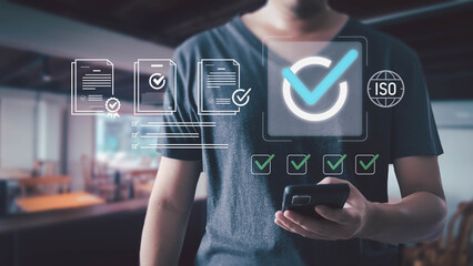 Man holding smartphone with virtual interface showing ISO certification and quality assurance documents with checkmarks. Concept of digital standards verification in modern business.