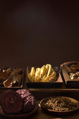 Vertical image of ginseng roots and herbs placed in bowls. Dark background with warm light emphasizes the texture and traditional theme. Copy space