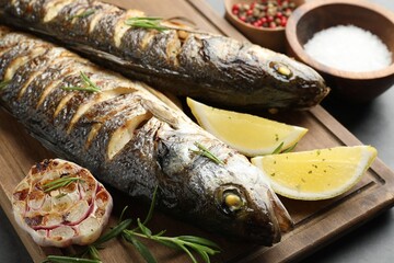 Tasty roasted seabass fish served with rosemary and lemon on grey table, closeup. Homemade seafood...