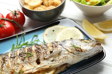Tasty roasted seabass fish served with potatoes on white wooden table, closeup. Homemade seafood dish
