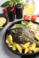 Tasty roasted flounder fish with herbs, potato and tomatoes on light table, closeup. Homemade seafood dish