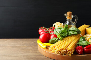 Raw spaghetti pasta and products on wooden table against black background, closeup. Space for text