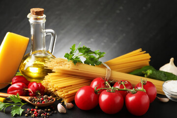 Raw spaghetti pasta, products and spices on black table against dark textured background, closeup