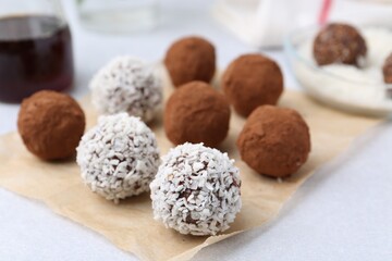 Delicious homemade candies with cocoa powder and coconut flakes on light table, closeup