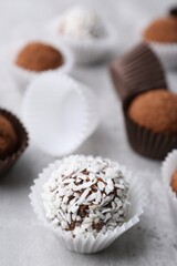 Delicious homemade candies with cocoa powder and coconut flakes on light grey table, closeup