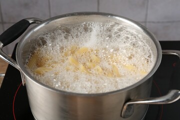 Fresh pasta boiling in pot with water on electric stove, closeup