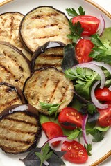 Grilled slices of eggplant with salad on white table, closeup