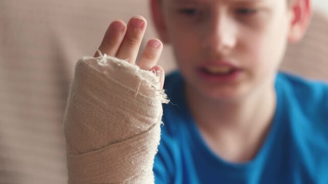 portrait of upset caucasian boy 11 years old with broken arm bandaged with plaster cast suffers from pain, first aid for arm fracture injury