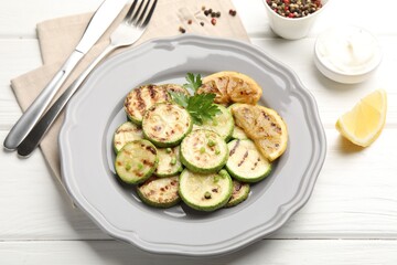 Delicious fried courgette slices with lemon and parsley served on white wooden table, closeup