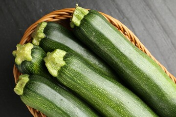 Fresh ripe zucchinis in wicker basket on black table, top view