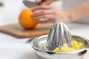 Making juice. Woman cutting orange at white marble table indoors, focus on juicer
