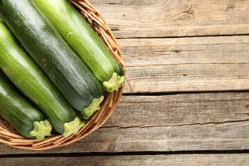 Fresh ripe zucchinis in wicker basket on wooden table, top view. Space for text