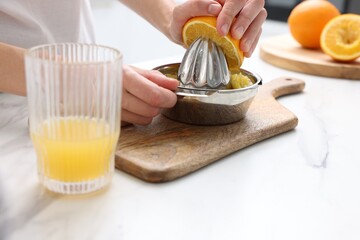 Making juice. Woman with orange using juicer at white marble table indoors, closeup