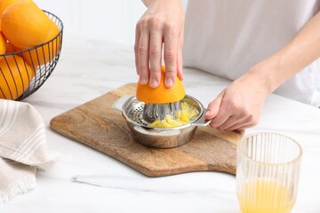 Making juice. Woman with orange using juicer at white marble table indoors, closeup