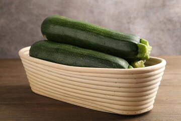 Fresh ripe zucchinis in wicker basket on wooden table, closeup