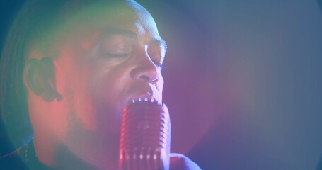 Singing male singer wearing dark shirt, holding retro microphone on stage with colored spotlights