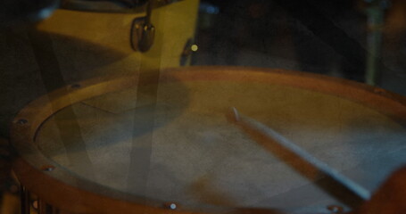 Hitting wooden snare drum with blurred drumsticks on dim stage, with warm lighting