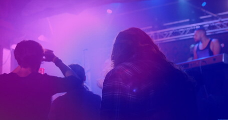 Watching long-haired man wearing plaid shirt shading eyes at music venue, with keyboard rig haze