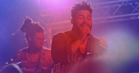 Performing mid adult singer gripping microphone, singing on concert stage, with guitar and fog haze