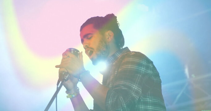Singing musician wearing green plaid shirt gripping mic at stand at concert stage, amid haze lights