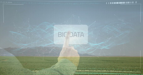 Reaching hand wearing green sleeve tapping BIG DATA button over crop field, digital interface