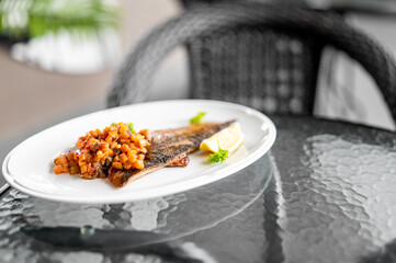 Grilled fish fillet with tomato salsa, lemon wedges, and parsley garnish served on a white plate...