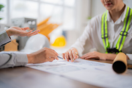 Two engineers are discussing a building project blueprint, pointing with a pen and gesturing with hands, showcasing teamwork and expertise in architectural design