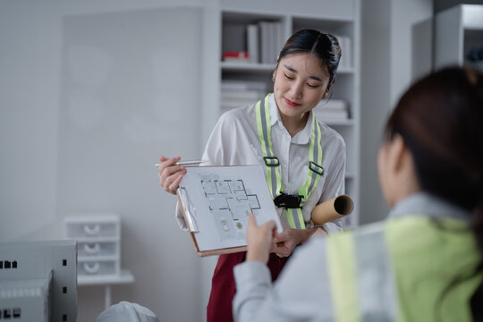 Two asian female architects are discussing a building project. Reviewing blueprints and architectural plans in the office. Sharing ideas and collaborating on design solutions for optimal construction