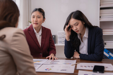 Asian businesswomen experiencing stress and frustration while discussing company performance and financial problems during meeting in office