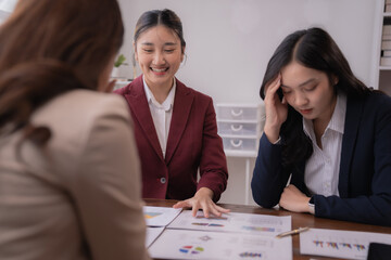 Asian businesswomen showing bad financial chart to colleagues during a meeting in the office, one of them is stressed and touching her forehead