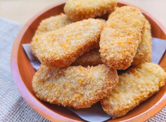 Close-up of fried chicken nuggets in a wooden plate are on the table. 