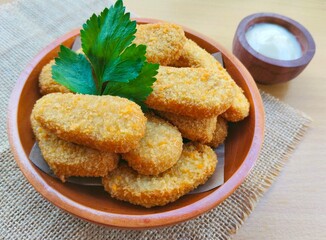 Fried chicken nuggets in a wooden plate and mayonnaise sauce in a small wooden bowl on the table.