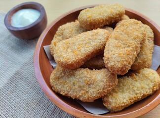 Fried chicken nuggets in a wooden plate and mayonnaise sauce in a small wooden bowl on the table.
