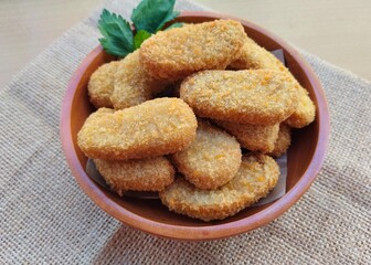 Fried chicken nuggets in a wooden plate are on the table. 