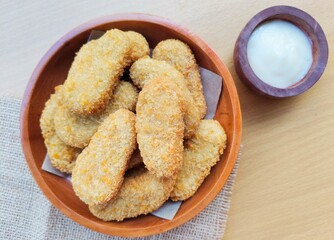 Fried chicken nuggets in a wooden plate and mayonnaise sauce in a small wooden bowl on the table.