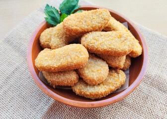 Fried chicken nuggets in a wooden plate are on the table.