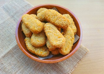 Fried chicken nuggets in a wooden plate are on the table.