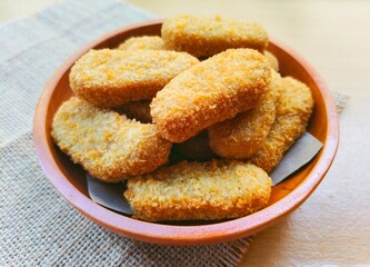 Fried chicken nuggets in a wooden plate are on the table.