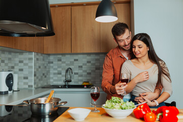 Couple enjoying time together in the kitchen, preparing fresh food and testing red wine. Domestic lifestyle with love, cooking, and shared moments at home