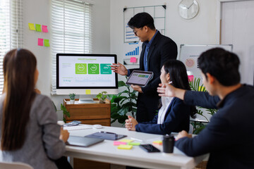 Asian businessman lead young group of multiethnic businesspeople in team meeting, using desktop computer for ESG topic presentation on monitor. Sustainable business practice, people work at office con