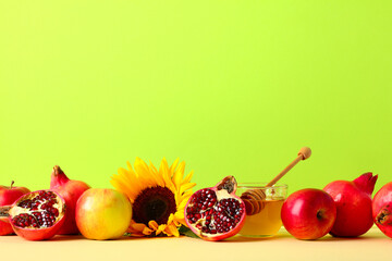 Rosh Hashanah still life with honey, apples, pomegranates, and sunflower on green background.