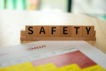 "Safety" English word block that placed with risk assessment checklist form on the table. Zero accident campaign in the high risk industrial working. Close-up.