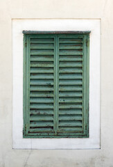 Close-up view of a rustic green shuttered window set within a worn white wall