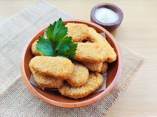 Fried chicken nuggets in a wooden plate and mayonnaise sauce in a small wooden bowl on the table.
