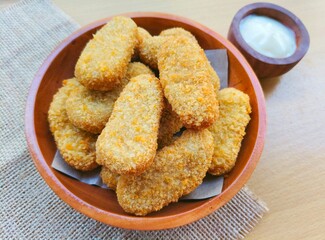 Fried chicken nuggets in a wooden plate and mayonnaise sauce in a small wooden bowl on the table.